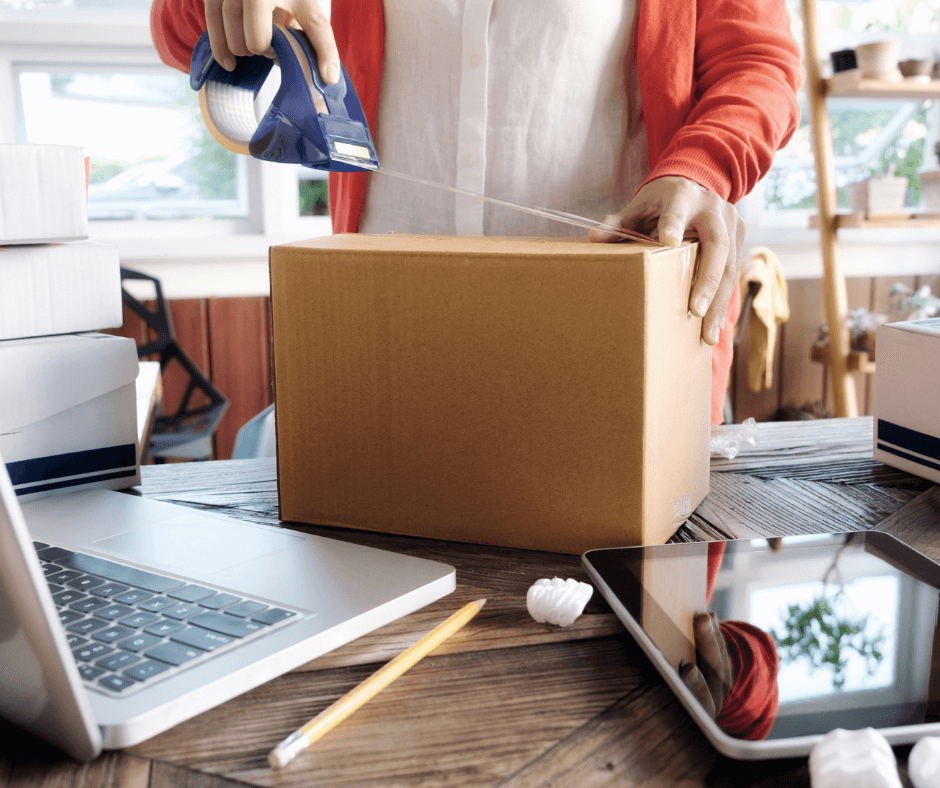 On the table, a man is packing a cardboard box with scotch tape